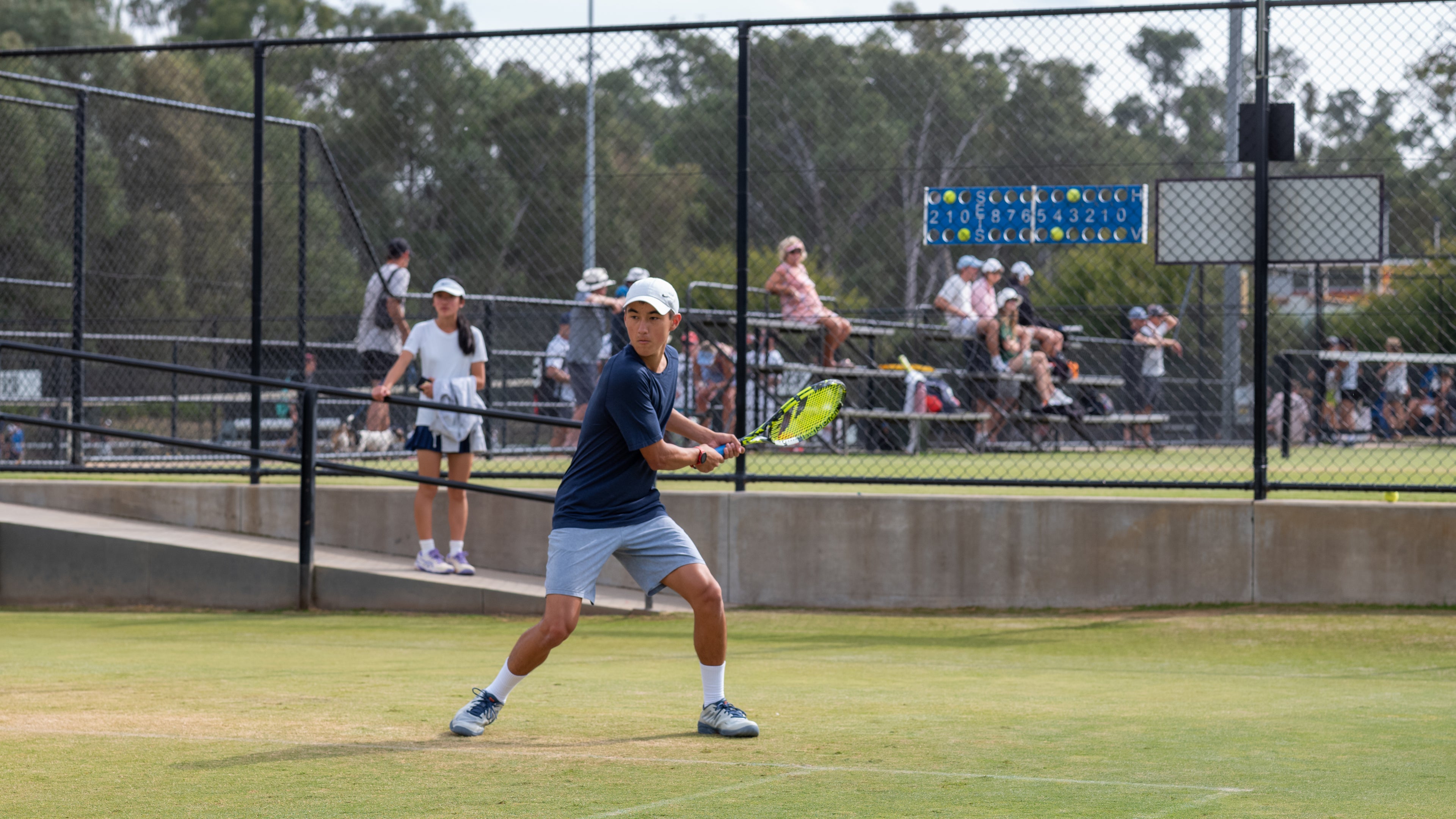 Tennis player in action on a grass court with spectators in the background