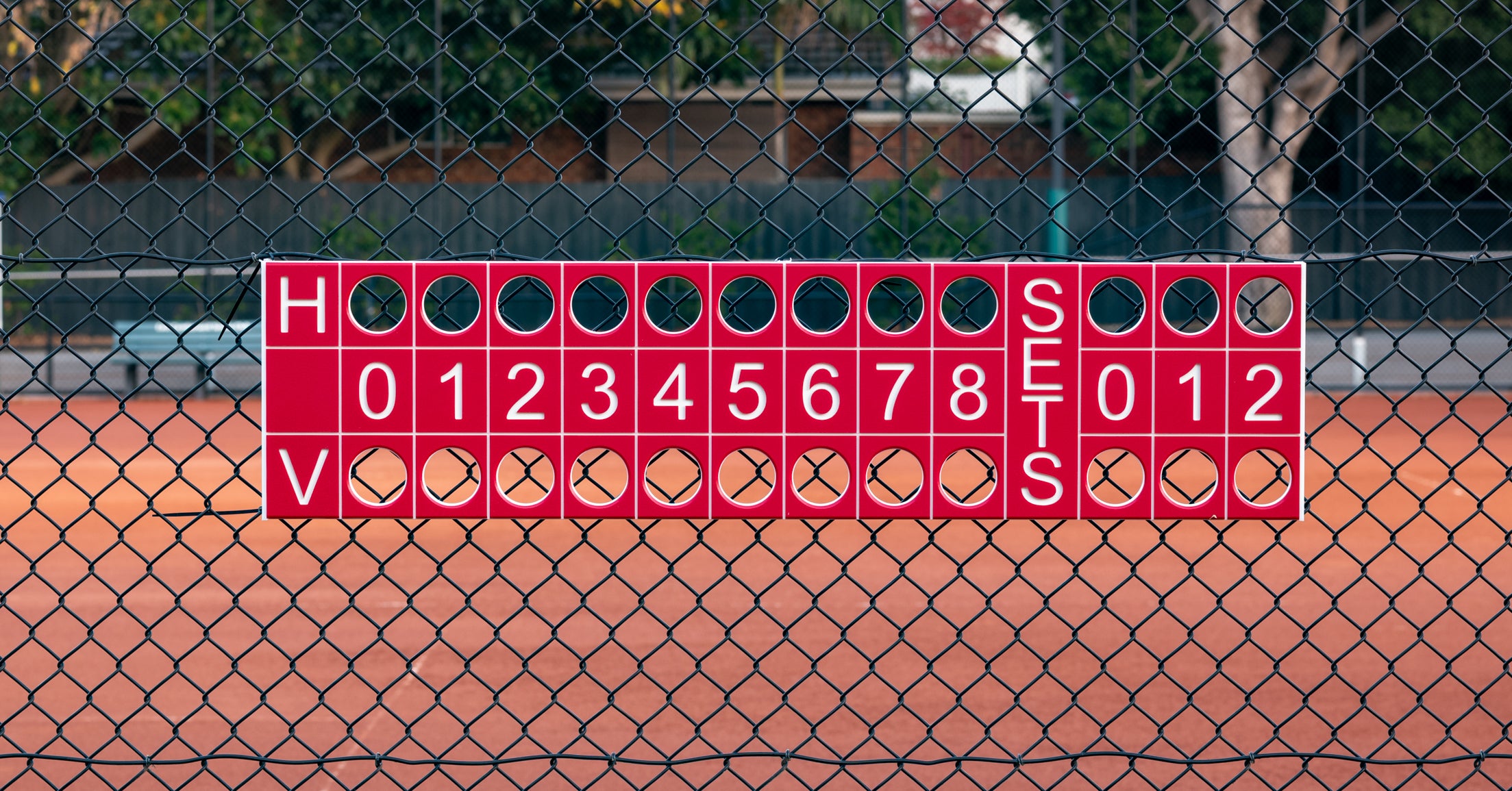 Tennis scoreboard on a chain-link fence with a tennis court background