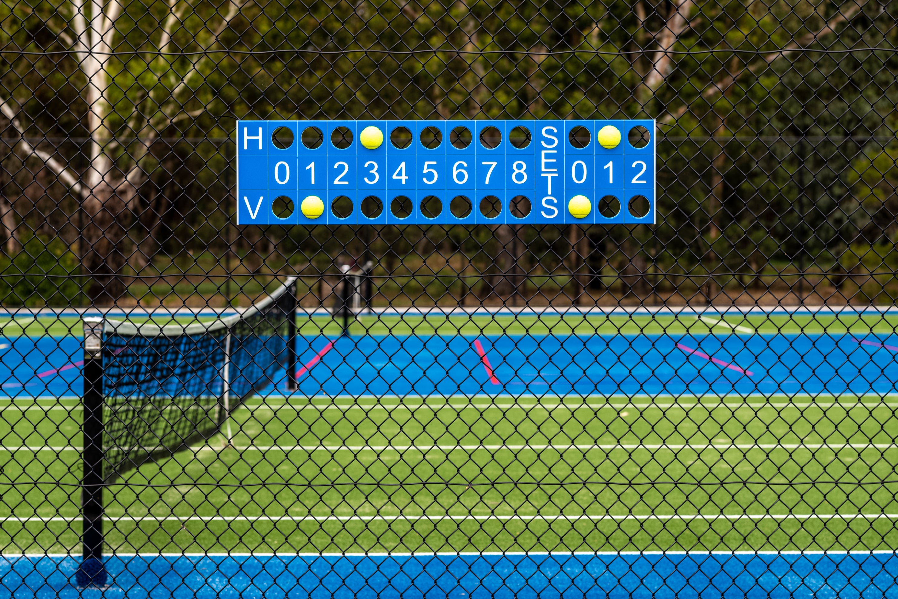 Tennis court with a scoreboard and net, surrounded by trees